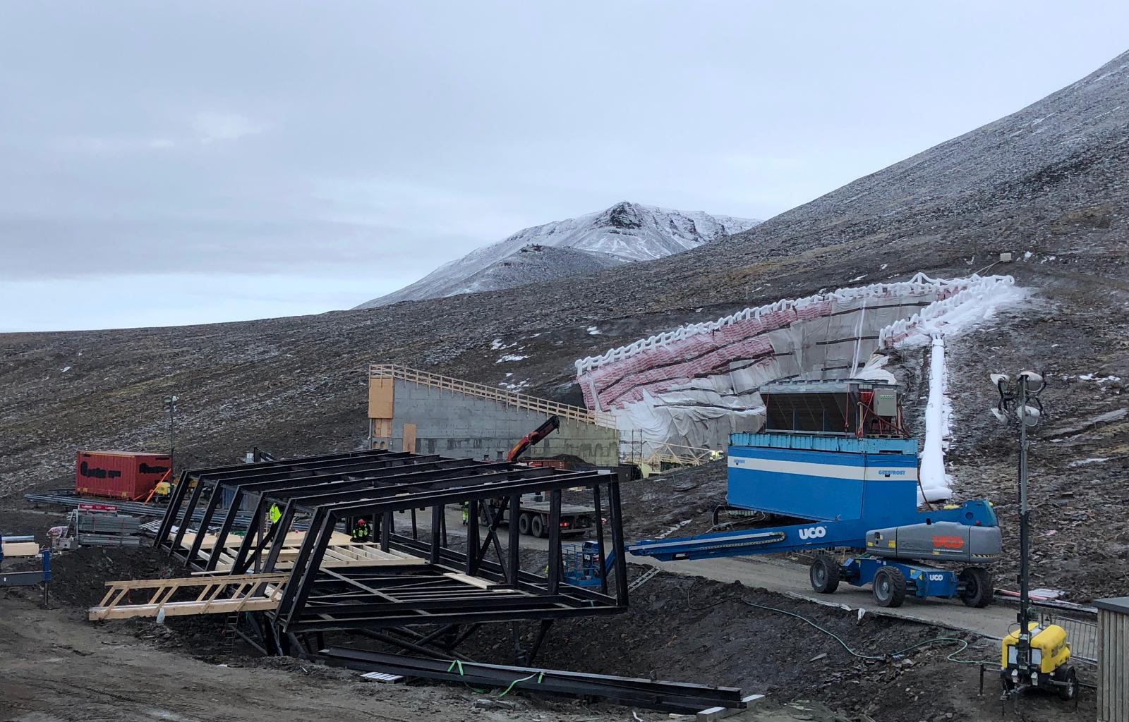 Rehabiliteringen og tettingen av Svalbard globale frøhvelv skal være ferdigstilt i mai/juni i år. Det nye servicebygget, til venstre i bildet, skal bidra til å redusere aktiviteten i  inngangstunnelen, og dermed redusere kuldetapet i hvelvet. (Foto: Statsbygg).