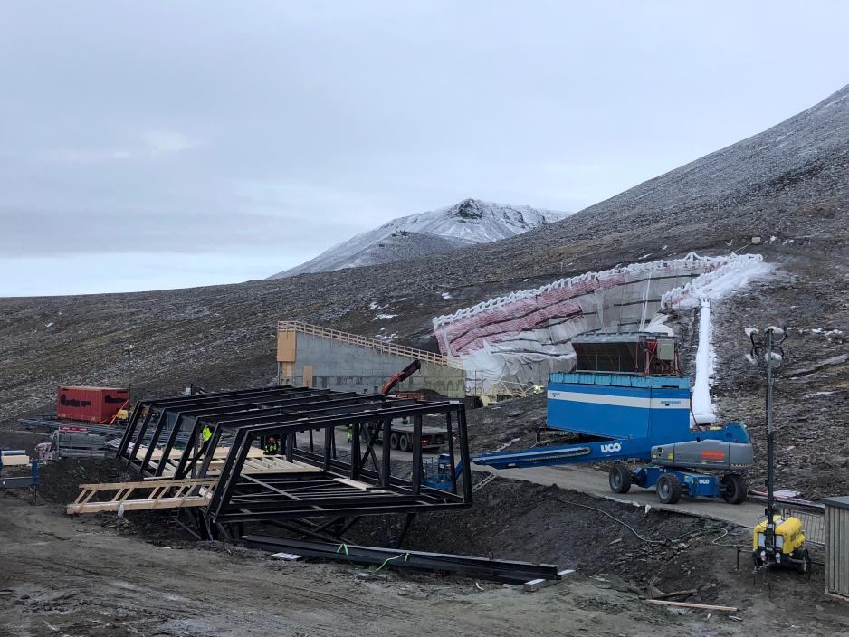 Rehabiliteringen og tettingen av Svalbard globale frøhvelv skal være ferdigstilt i mai/juni i år. Det nye servicebygget, til venstre i bildet, skal bidra til å redusere aktiviteten i  inngangstunnelen, og dermed redusere kuldetapet i hvelvet. (Foto: Statsbygg).