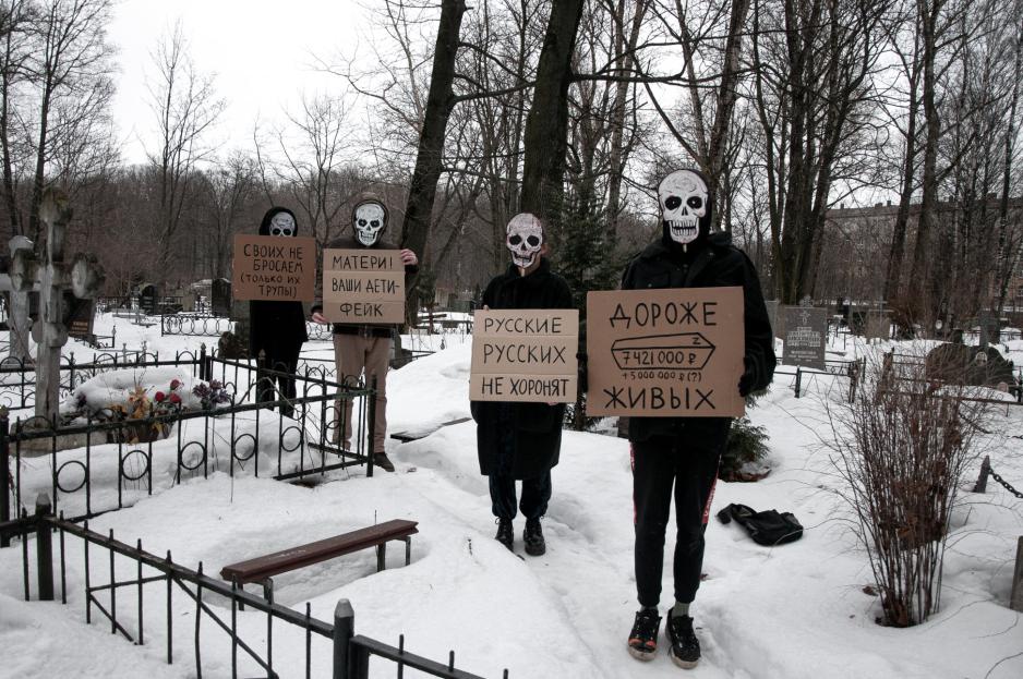 Medlemmer av De dødes parti (Партия мёртвых), en russisk kunstnerisk protestgruppe, demonstrerer mot krigen i Ukraina på en kirkegård i St. Petersburg. På plakatene fra venstre kan man lese «Своих не бросаем (только их tрупы)» – «Vi forlater ikke våre egne (bare likene deres)»; «Матери! Ваши дети фейк» – «Mødre! Deres barn er fake»; «Русские русских не хоронят» – «Russere begraver ikke russere»; «Дороже живых» – «Mer verdifulle enn de levende». (Foto: De dødes parti). Medlemmer av De dødes parti en russisk kunstnerisk protestgruppe, demonstrerer mot krigen i Ukraina på en kirkegård i St. Petersburg