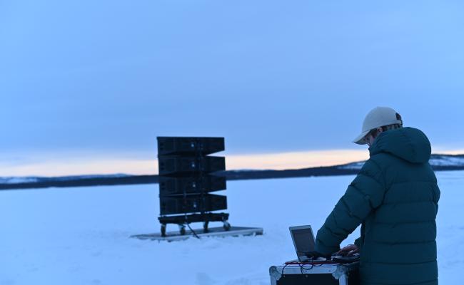 I slutten av februar 2022 ble Barents Spektakel avrundet med symboltung stillhet fra russisk side av Pasvikelva. Som et verk om lytting og brobygging over store avstander, skulle den norske kunstneren Tine Surel Lange (på bildet) og hennes russisk-ukrainske kollega Pavlo Grazhdanskij spille av tåkesignaler til hverandre over grenseelva ved hjelp av kraftige høyttalere. Lyden av tåkeluren fra norsk side fikk ingen gjenklang da russiske myndigheter brått satte en stopper for framføringen. På årets Spektakel deler de to kunstnerne sine refleksjoner rundt tillit. (Foto: Ingrid Fadnes)