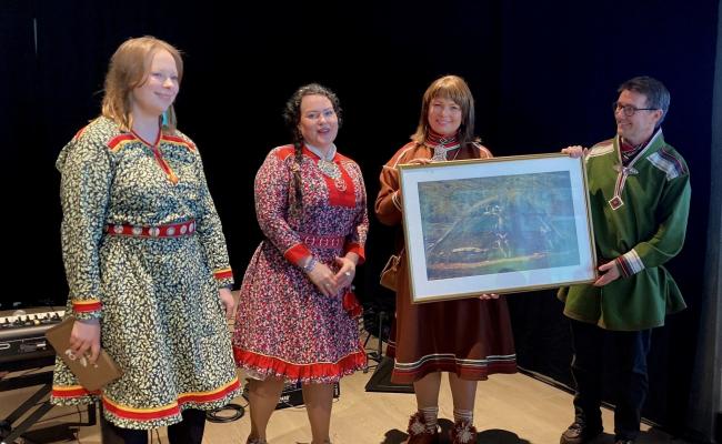 Sametingspresident Silje Karine Muotka (andre t.v.) og Sandra Márjá West, politisk rådgiver for sametingsrådet (ytterst t.v.), var til stede på åpningen av Samisk hus i Tromsø/Romssa Sámi Viessu. Her overrekker de en gave fra Sametinget til huset ved daglig leder Jill Abelsen Olsen og styreleder Torjer Olsen. Dette er et fotografi fra den gamle samiske sommerboplassen i Romsavággi/Tromsdalen fra rundt år 1920. Bildet er tilrettelagt av den samiske kunstneren Hans Ragnar Mathisen. (Foto: Sametinget) Sametingspresident Silje Karine Muotka (andre t.v.) og Sandra Márjá West, politisk rådgiver for sametingsrådet (ytterst t.v.), var til stede på åpningen av Samisk hus i Tromsø/Romssa Sámi Viessu. Her overrekker de en gave fra Sametinget til huset ved daglig leder Jill Abelsen Olsen og styreleder Torjer Olsen. Dette er et fotografi fra den gamle samiske sommerboplassen i Romsavággi/Tromsdalen fra rundt år 1920. Bildet er tilrettelagt av den samiske kunstneren Hans Ragnar Mathisen. (Foto: Sametinget)