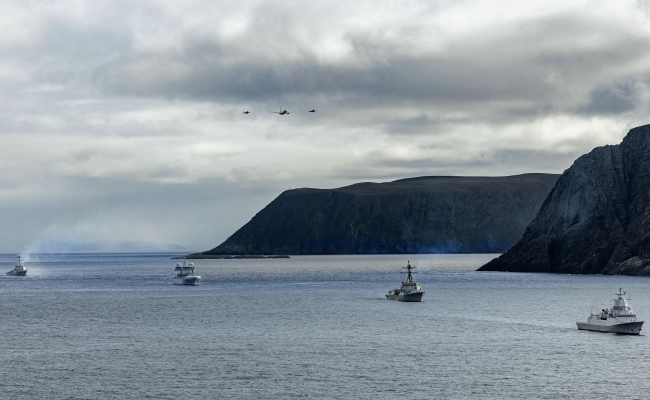 The Arleigh Burke-class guided missile destroyer USS Mahan (DDG 72), left, Royal Norwegian replenishment oiler HNoMS Maud (A-530), second to left, USS Bainbridge (DDG 96), right, and Royal Norwegian Navy Fridtjof Nansen-class frigate HNoMS Thor Heyerdahl (F-314), transit the North Cape fjord in the Barents Sea above the Arctic Circle as a Royal Norwegian Air Force P-8 Poseidon, flanked by two Royal Norwegian Air Force F-35 Lightning IIs fly overhead, Aug. 29, 2025. (Source: U.S. Navy Photo by Mass Communication Specialist 2nd Class Alice Husted) Nordkapp Patrol